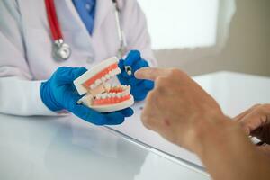 tandläkare rekommendera sätt behandla problem tänder och tandläkare också ge råd patienter känna till ta vård av deras tänder efter behandling är avslutad. tandläkare innehav proteser i hand och talande till patient foto