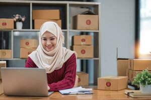 muslim kvinna uppkopplad Lagra små företag ägare säljare entreprenör förpackning paket posta frakt låda framställning leverans paket på tabell. e-handel släppa frakt sändning service begrepp. foto