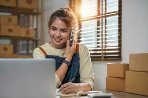 småföretagare sme frilansande kvinna som använder telefonsamtal ta emot från kund som kontrollerar produkt på lager på hemmakontoret, onlinemarknadsföring förpackningsleveranslåda, sme e-handelskoncept. foto