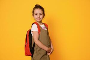 förtjusande liten barn flicka 6 år gammal, primär skola unge, först väghyvel med ryggsäck, leende sött ser på kamera foto