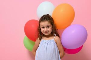 isolerat porträtt av skön Söt glad 4 år bebis flicka med flerfärgad ballonger leende ser på kamera. rosa bakgrund, Plats för text, reklam fotografi foto