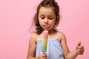 huvudskott 4 år Söt bebis flicka med friska vegan is grädde isglass i hand och som visar tumme upp.rosa bakgrund, kopia Plats . sommar efterrätt, glad sommar humör begrepp foto