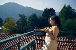 ton porträtt av en skön kvinna dricka friska juice i de terrass eller balkong, mot de italiensk alps bakgrund foto