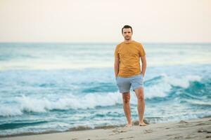 ung man gående på de strand på solnedgång foto