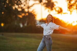 porträtt av Lycklig ung kvinna utomhus- i de parkera på solnedgång foto