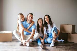 Lycklig familj med två döttrar med kartong lådor i ny hus på rör på sig dag foto