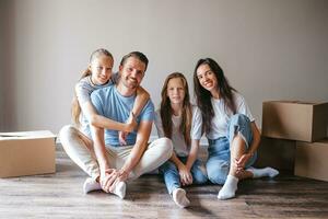 Lycklig familj med två döttrar med kartong lådor i ny hus på rör på sig dag foto