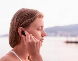 kvinna som använder trådlösa hörlurar, havet i bakgrunden