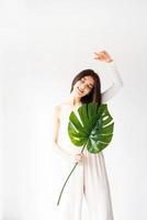 glad vacker kvinna i mysiga kläder som håller ett grönt monstera blad foto