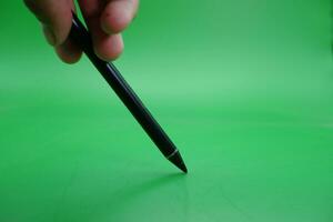 en svart nål penna varelse hölls över en grön bakgrund. foto