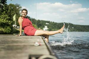 Lycklig kvinna Sammanträde på brygga på en sjö foto