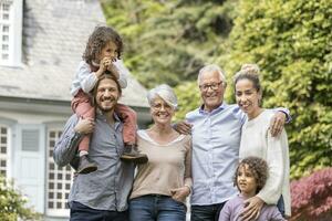 Lycklig utökad familj stående i trädgård av deras Hem foto