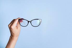 glasögon i kvinna hand på blå bakgrund. optisk Lagra, syn testa, eleganta glasögon begrepp foto