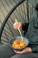 udon spaghetti med räka och friterad grönsaker i en skål i kvinna händer med ätpinnar foto