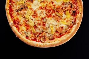italiensk pizza med skivad skinka och kronärtskocka på svart bakgrund foto