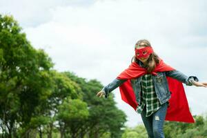 på en skön dag i de parkera, en ung flicka åtnjuter henne semester. lekfull med en röd superhjälte kostym och mask. foto