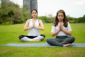 ung kvinna och liten flicka med utomhus- aktiviteter i de stad parkera, yoga är henne VALDA aktivitet. foto