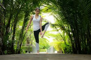 ung kvinna i de trädgård där är trä- gångvägar och en tunnel av färsk grön träd, med yoga aktiviteter för hälsa foto