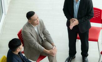 självsäker asiatisk affärsman Sammanträde på stol och talande med hans kollega i kontor foto