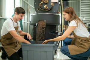 ung man och kvinna arbetssätt i kaffe bönor stekare, de är kontroll av kaffe bönor rostad. foto