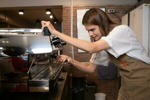 ung kvinna Barista framställning kaffe i Kafé. kvinna Barista använder sig av kaffe maskin. foto