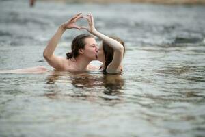 två ung flickor i de vatten framställning en hjärta med deras händer. foto