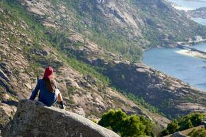 flicka med röd keps är på en sten på de topp av de berg utsikt de atlanten kust. foto