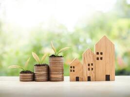 miniatyr- hus och växter växande upp på stack av mynt för investering fast egendom begrepp. sparande pengar för köpa en hus. foto