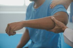 läkare eller fysioterapeut arbetssätt granskning behandla skadade ärm av idrottare manlig patient, stretching och träning, håller på med de rehabilitering terapi smärta i klinik. foto