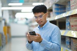 asiatisk man i de mataffär handla använder sig av mobil telefon och leende i mataffär bakgrund. detaljhandeln begrepp. små företag foto