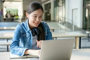 skön asiatisk kvinna kvinna studerande upphetsad kontroll språk testa resultat på bärbar dator. leende flicka Lycklig studie uppkopplad. bok i högskola campus. porträtt kvinna på internationell Asien universitet. foto