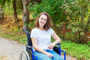 ung Lycklig handikapp kvinna i rullstol på väg i sjukhus parkera väntar för patient tjänster. lam flicka i ogiltig stol för Inaktiverad människor utomhus- i natur. rehabilitering begrepp. foto
