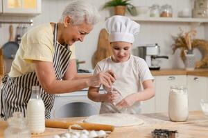 Lycklig familj i kök. mormor och barnbarn barn laga mat i kök tillsammans. mormor undervisning unge flicka knåda deg baka småkakor. hushåll lagarbete portion familj generationer begrepp. foto