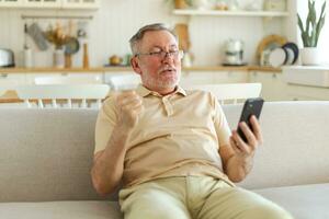 mitten åldrig senior man euforisk vinnare med smartphone. äldre mogna farfar ser på cell telefon läsning bra Nyheter få Bra resultat vinnande uppkopplad bud känsla förvånad. vinnande gest. foto