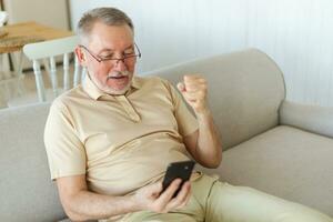 mitten åldrig senior man euforisk vinnare med smartphone. äldre mogna farfar ser på cell telefon läsning bra Nyheter få Bra resultat vinnande uppkopplad bud känsla förvånad. vinnande gest. foto