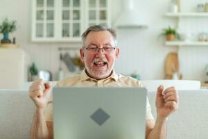 upphetsad mitten åldrig senior man euforisk vinnare. äldre mogna farfar ser på bärbar dator läsning bra Nyheter få Bra resultat vinnande uppkopplad bud känsla förvånad. vinnande gest. foto