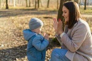 Lycklig familj utomhus. mor barn på promenad i parkera. mamma spelar med bebis son utomhus. kvinna liten bebis pojke vilar gående i natur. liten litet barn barn och barnvakt barnskötare har roligt tillsammans. foto