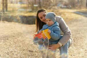 Lycklig familj utomhus. mor barn på promenad i parkera. mamma spelar med bebis son utomhus. kvinna liten bebis pojke vilar gående i natur. liten litet barn barn och barnvakt barnskötare har roligt tillsammans. foto