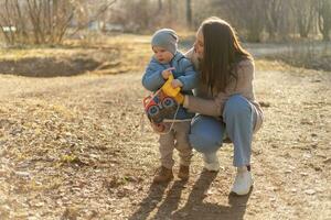 Lycklig familj utomhus. mor barn på promenad i parkera. mamma spelar med bebis son utomhus. kvinna liten bebis pojke vilar gående i natur. liten litet barn barn och barnvakt barnskötare har roligt tillsammans. foto