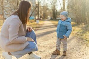 Lycklig familj utomhus. mor barn på promenad i parkera. mamma spelar med bebis son utomhus. kvinna liten bebis pojke vilar gående i natur. liten litet barn barn och barnvakt barnskötare har roligt tillsammans. foto