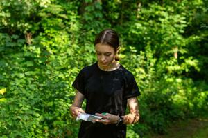 ung flicka i skog läsning Karta och sökande för en kontrollera punkt. sporter orientering konkurrens. foto