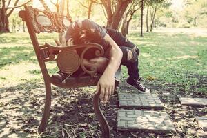 ung man som sover på bänken utomhus i stadsparken under dagen foto