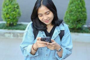 sorglös leende eleganta asiatisk ung kvinna använder sig av smartphone app, video chatt, uppkopplad affär, och bläddring social media ha på sig tillfällig i utomhus- foto