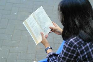 Lycklig uppmärksam ung asiatisk kvinna högskola studerande läsning en bok i de parkera, utbildning begrepp foto
