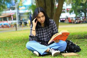 omtänksam kvinna asiatisk studerande läsning en bok och tänkande till planera en projekt foto