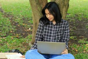 ung leende asiatisk kvinna använder sig av bärbar dator och skrivning anteckningsbok, glad asiatisk studerande tittar på webinar och studerar från e kurs foto