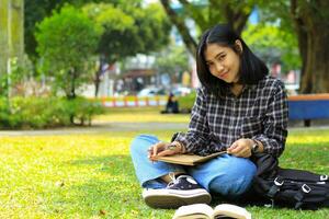 smart Lycklig ung asiatisk kvinna leende och skrivning schema i anteckningsbok med en penna studie för examen ser på kamera foto