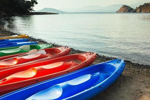 färgglada kanotbåtar på stranden, havet och bergen i bakgrunden