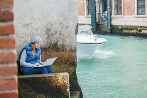 ung kvinna använder sig av bärbar dator förbi de kanal i Venedig foto