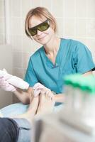 leende kosmetolog arbetar med laser för att behandla fötter foto